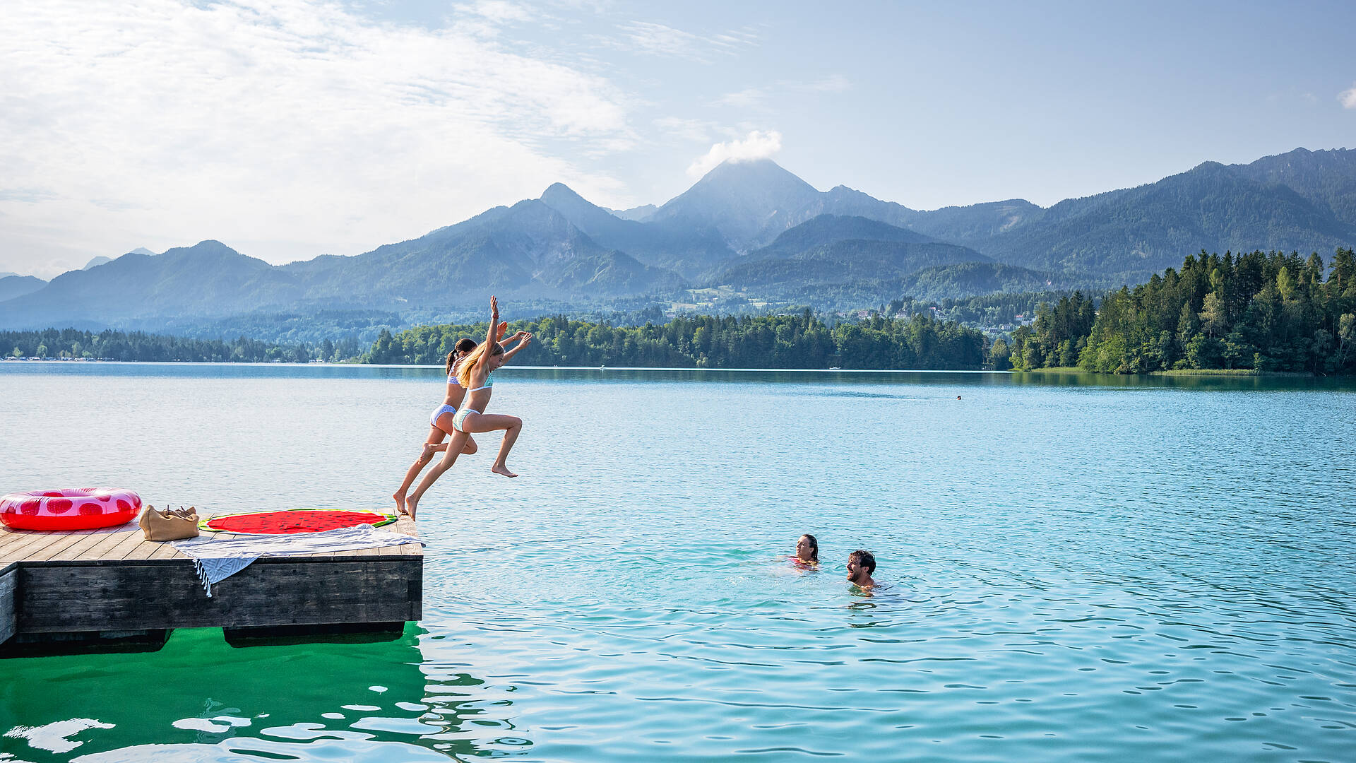 Kinder springen voller Begeisterung ins Wasser des Faaker Sees.