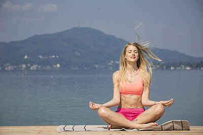 Junge Frau sitzt am Steg im Strandbad Wörthersee und macht Yoga